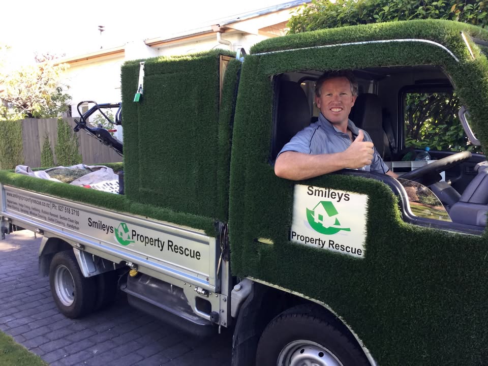 Smileys Property Rescue operator giving a thumbs up from the cab of the turf-covered work ute, with the company logo on the door panel